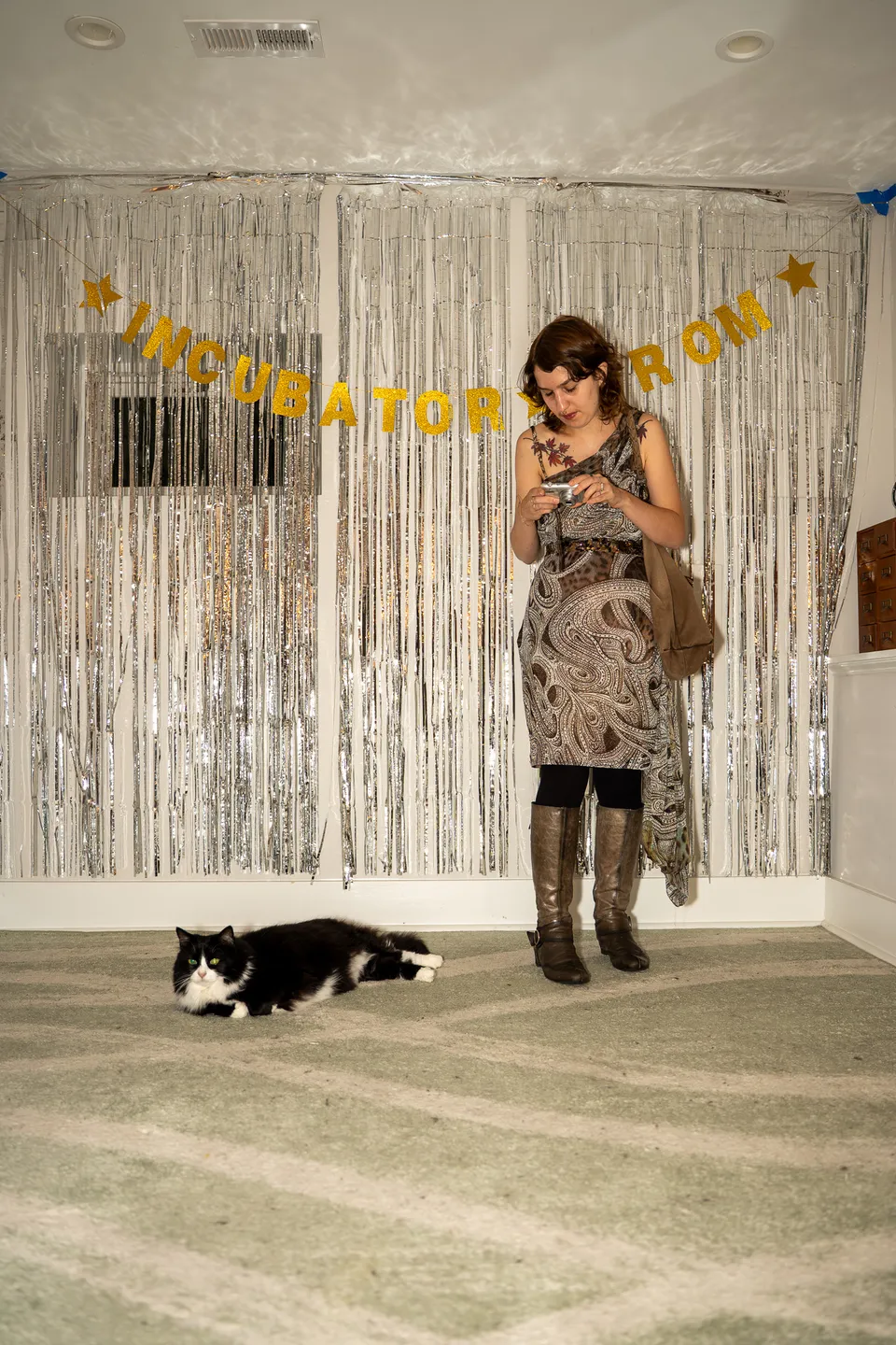 Guest standing before the Incubator Prom backdrop while a cat lounges on the rug