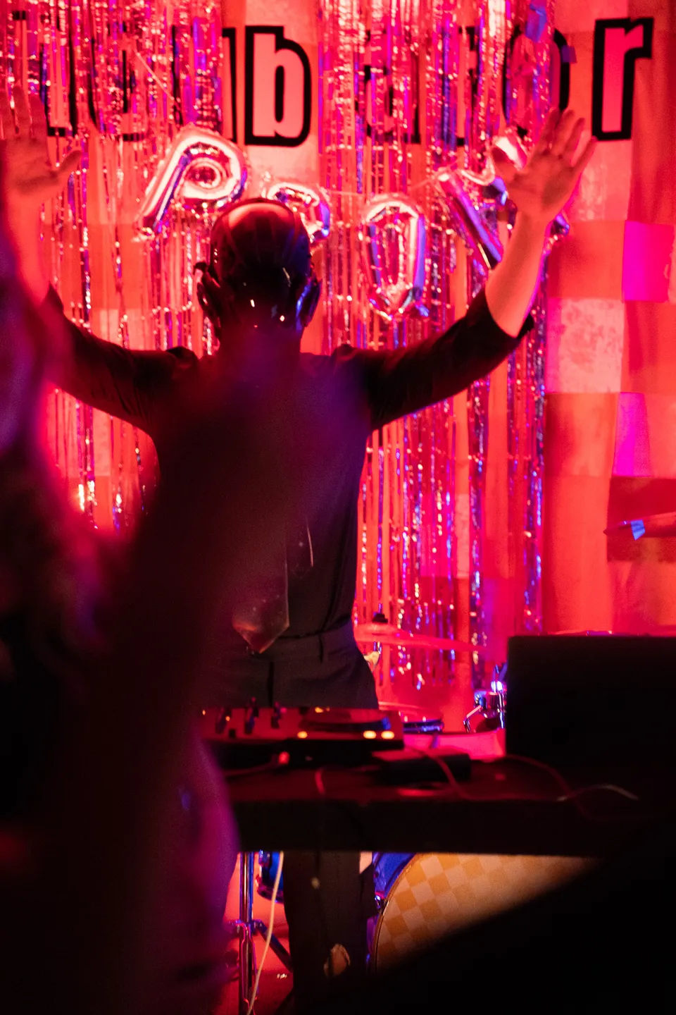 DJ with arms raised in front of a red-lit Incubator Prom sign
